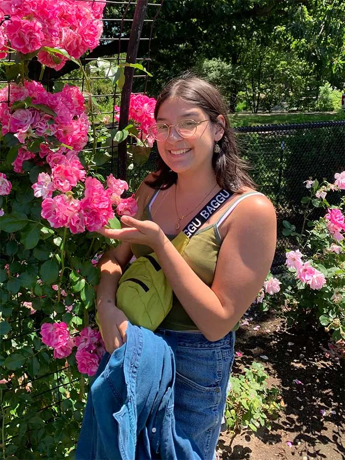 female student with shoulder length dark hair standing next to pink flowering shrub