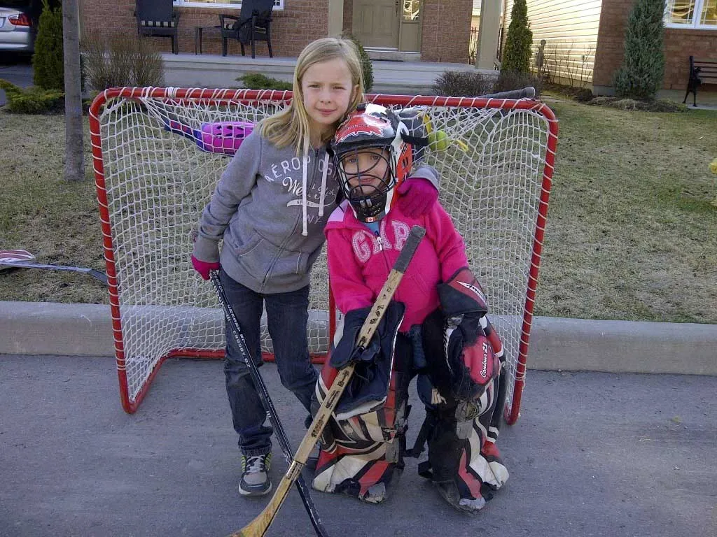 two young girls standing in front of a hockey net one holding a hockey stick