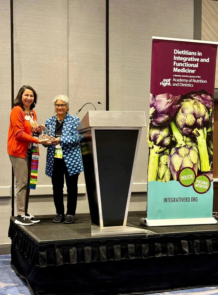 One woman handing award to another at a podium