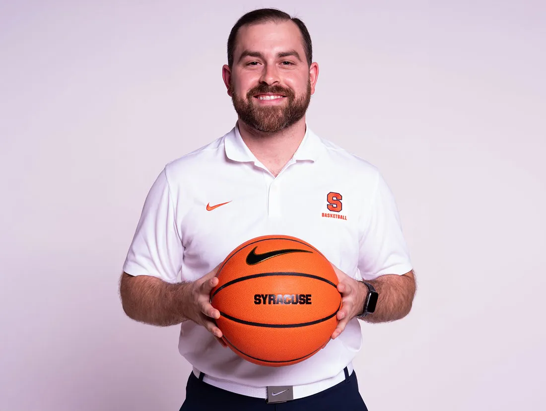 Mike Mangano in white SU shirt holding a basketball in front of him