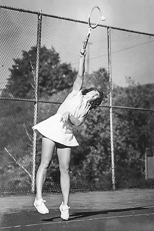 black and white image of Abbe Seldin reaching over her head to his the ball in a tennis match