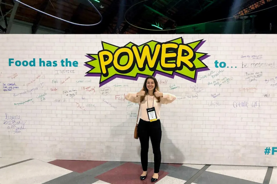 female students stands in front of a wall with graffiti writing that says Power