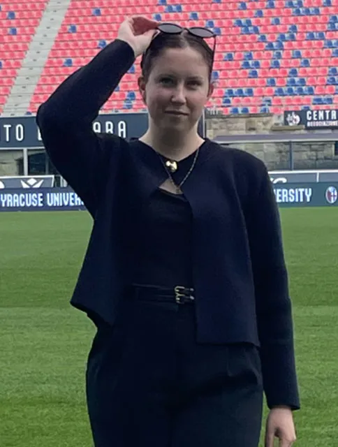 Anna Meara Pierce standing on athletic field holding her sunglasses to her head